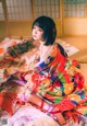 A woman in a colorful kimono sitting on a bed.