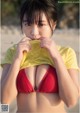 A woman in a red bikini holding a yellow shirt over her mouth.