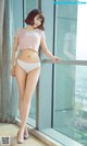 A woman in a pink top and white panties leaning against a window.