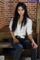 A woman sitting on a wooden bench in front of a brick wall.